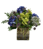Arreglo Floral de Hydrangeas en Tonos Lila y Follajes Artificiales en Base de Vidrio con Agua Acrílica