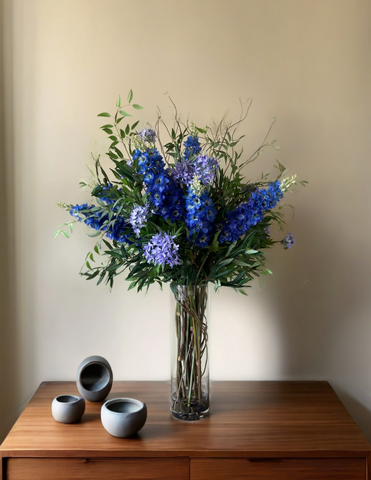 Arreglo Floral de Delphiniums y Agapanthus con Follajes Artificiales en Florero de Vidrio