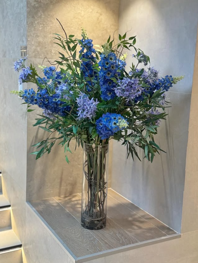 Arreglo Floral de Delphiniums y Agapanthus con Follajes Artificiales en Florero de Vidrio