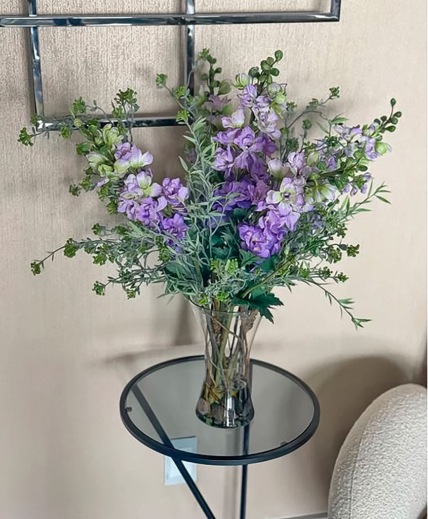 Arreglo Floral de Delphinium Lilas con Follajes Artificiales en Florero de Vidrio (Única Pieza)