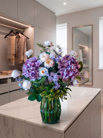 Arreglo Floral con Camelias, Hydrangeas Lilas y Follajes Artificiales en Florero de Vidrio y Agua Acrílica