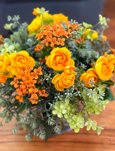 Arreglo Floral con Ranunculus Amarillos y Kalanchoes Naranjas Artificiales en Base Cuadrada de Vidrio y Agua Acrílica