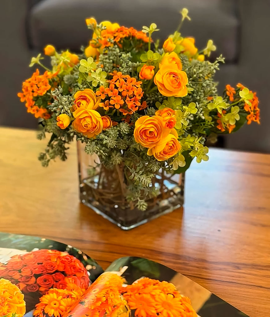 Arreglo Floral con Ranunculus Amarillos y Kalanchoes Naranjas Artificiales en Base Cuadrada de Vidrio y Agua Acrílica