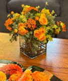 Arreglo Floral con Ranunculus Amarillos y Kalanchoes Naranjas Artificiales en Base Cuadrada de Vidrio y Agua Acrílica