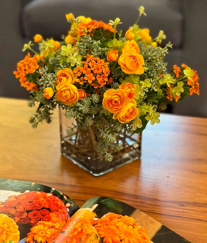 Arreglo Floral con Ranunculus Amarillos y Kalanchoes Naranjas Artificiales en Base Cuadrada de Vidrio y Agua Acrílica