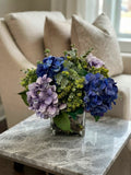 Arreglo Floral con Hydrangeas y Follajes Artificiales en Base Cuadrada de Vidrio con Agua Acrílica