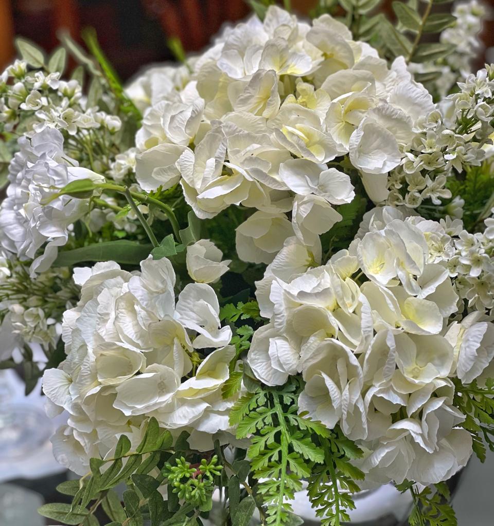 Centro de Mesa con Hydrangeas en Tonos Blancos y Follajes Artificiales en Base de Vidrio Tipo Espejo.