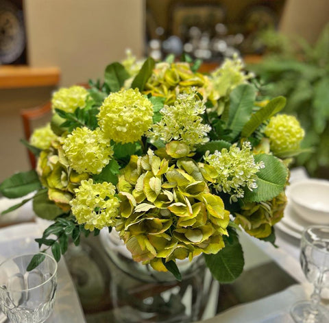 Centro de Mesa con Hydrangeas en Tonos Verdes y Follajes Artificiales en Base de Vidrio Tipo Espejo.