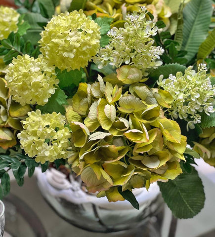 Centro de Mesa con Hydrangeas en Tonos Verdes y Follajes Artificiales en Base de Vidrio Tipo Espejo.
