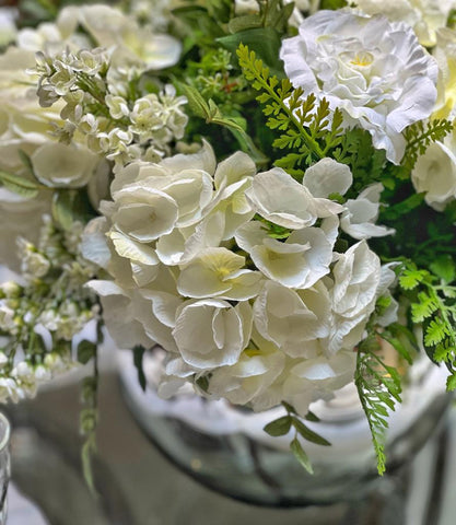 Centro de Mesa con Hydrangeas en Tonos Blancos y Follajes Artificiales en Base de Vidrio Tipo Espejo.