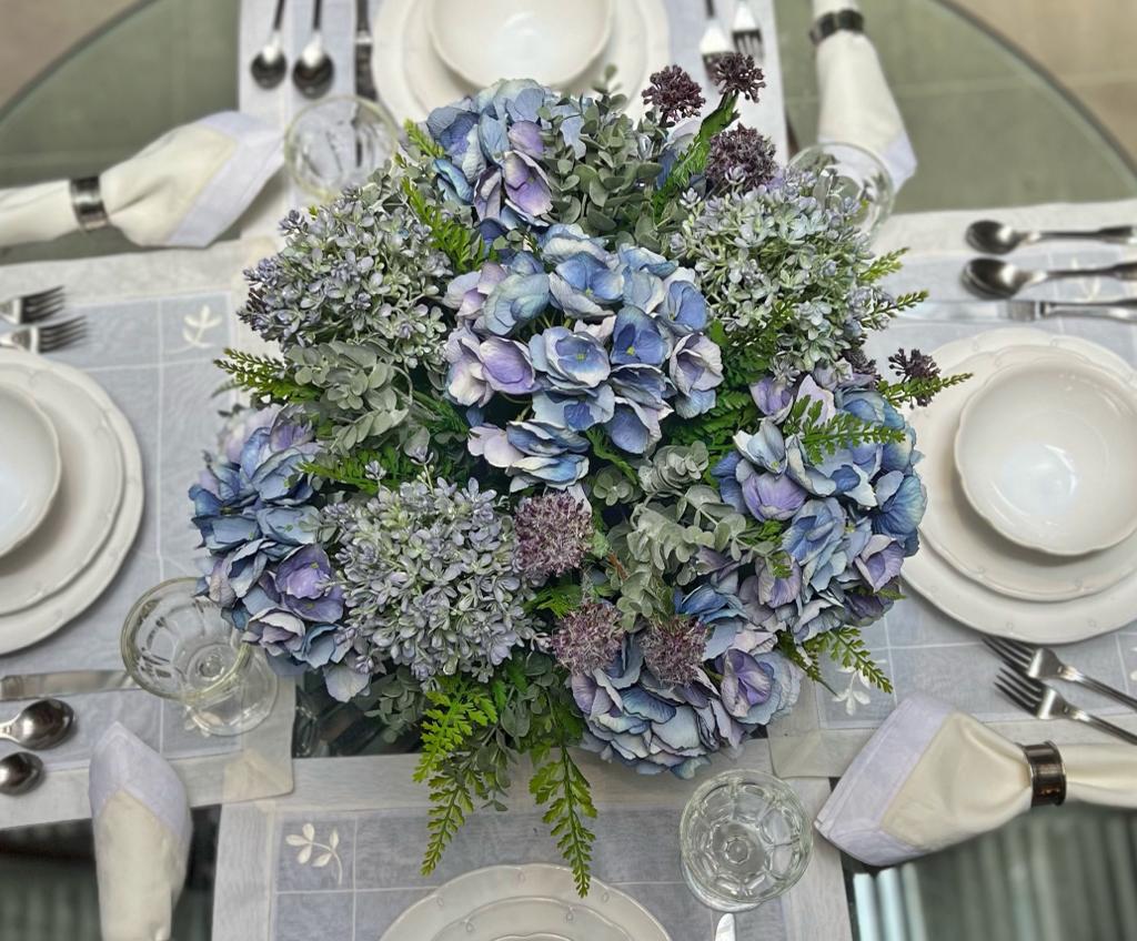 Centro de Mesa con Hydrangeas en Tonos Azules y Follajes Artificiales en Base de Vidrio Tipo Espejo.