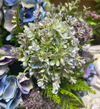 Centro de Mesa con Hydrangeas en Tonos Azules y Follajes Artificiales en Base de Vidrio Tipo Espejo.