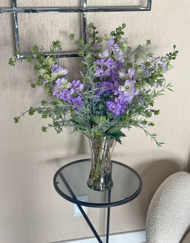Arreglo Floral con Delphiniums Lilas y Follajes Artificiales en Florero de Vidrio