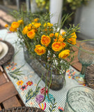 Centro de Mesa con Ranunculus y Follajes Artificiales en Base Ovalada de Vidrio