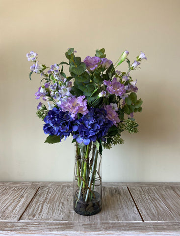Arreglo Floral con Lisianthus e Hidrangeas y Follajes Artificiales en Florero de Vidrio