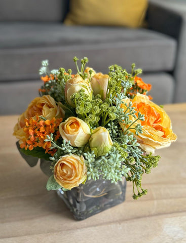 Arreglo Floral con Rosas Amarillas y Follajes Artificiales en Base Cuadrada de Vidrio