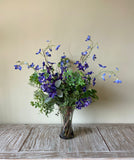 Arreglo Floral con Delphinium Azul y Follajes Artificiales en Florero de Vidrio