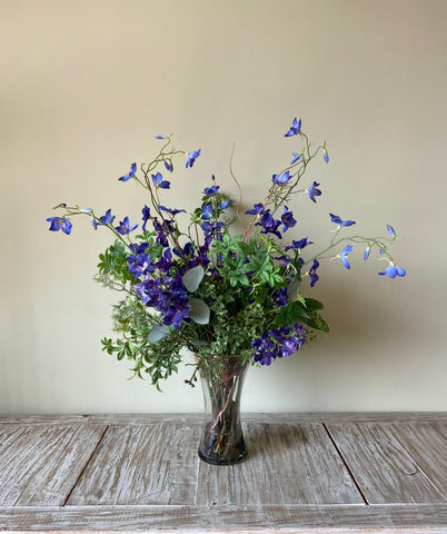Arreglo Floral con Delphinium Azul y Follajes Artificiales en Florero de Vidrio
