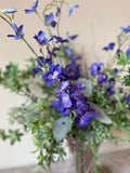 Arreglo Floral con Delphinium Azul y Follajes Artificiales en Florero de Vidrio