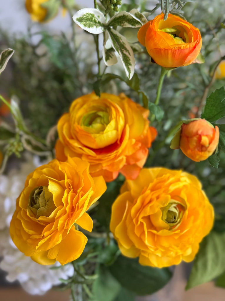 Arreglo Floral con Ranunculus Amarillos y Follajes Artificiales en Florero de Vidrio