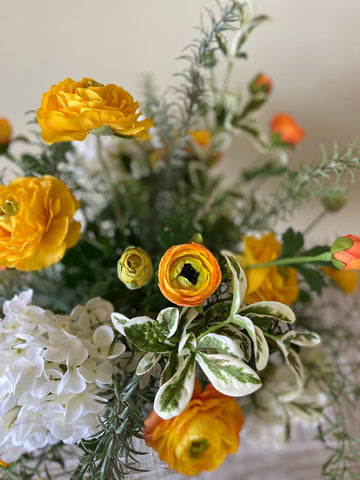 Arreglo Floral con Ranunculus Amarillos y Follajes Artificiales en Florero de Vidrio