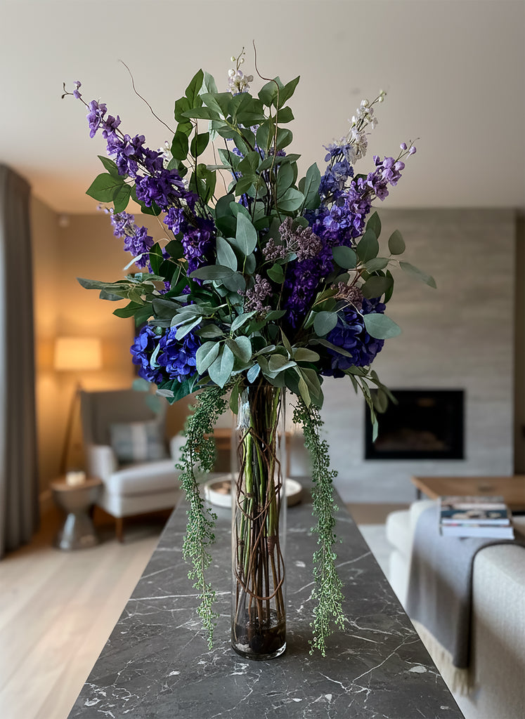 Arreglo Floral de Delphiniums e Hidrangeas con Follajes Artificiales en Cilindro de Vidrio