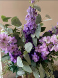 Arreglo Floral con Delphinium Lila y Follajes Artificiales en Florero de Vidrio