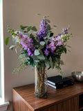 Arreglo Floral con Delphinium Lila y Follajes Artificiales en Florero de Vidrio