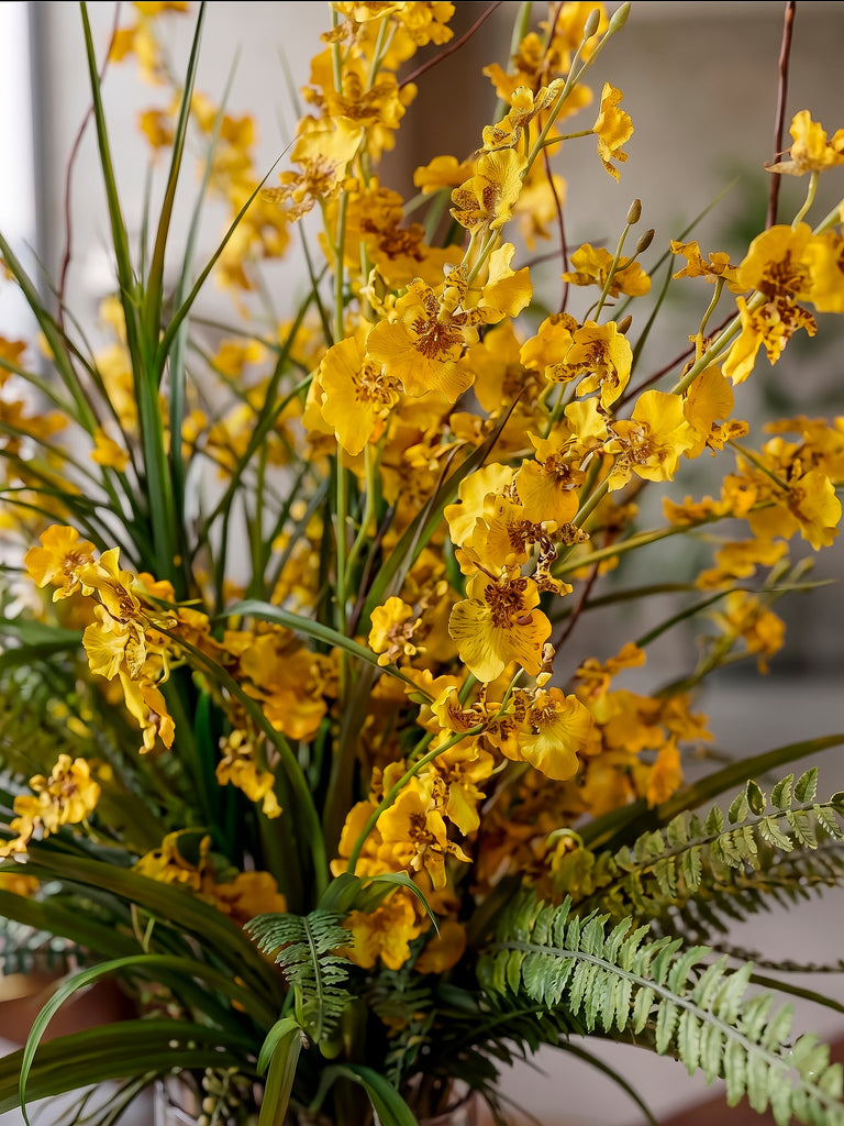 Orquideario con Oncidium Amarilla y Follajes Artificiales en Florero de Vidrio