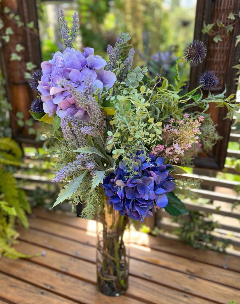 Arreglo Floral de Hydrangeas Lavandas y Follajes Artificiales en Cilindro de Vidrio con Agua Acrílica